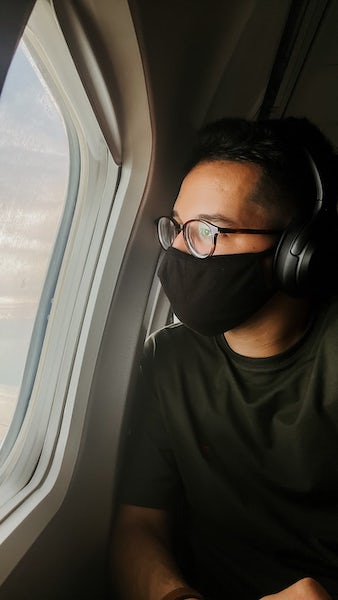 Man wearing a mask and headphones looking out the window of a plane.jpeg
